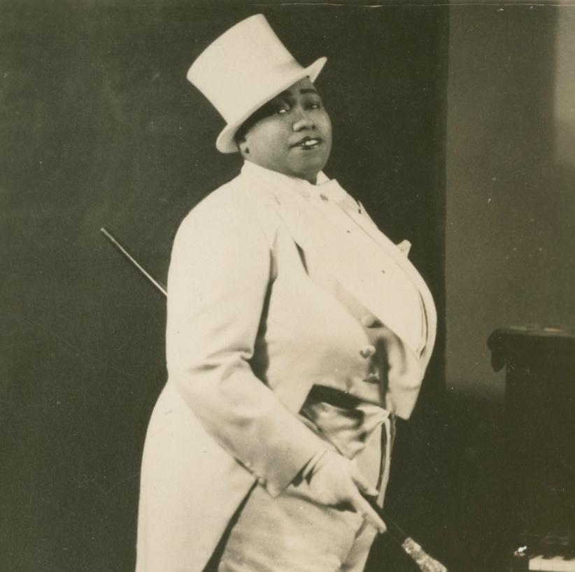 woman in a white suit and jacket with tails and a top hat, carrying a cane with a glass top