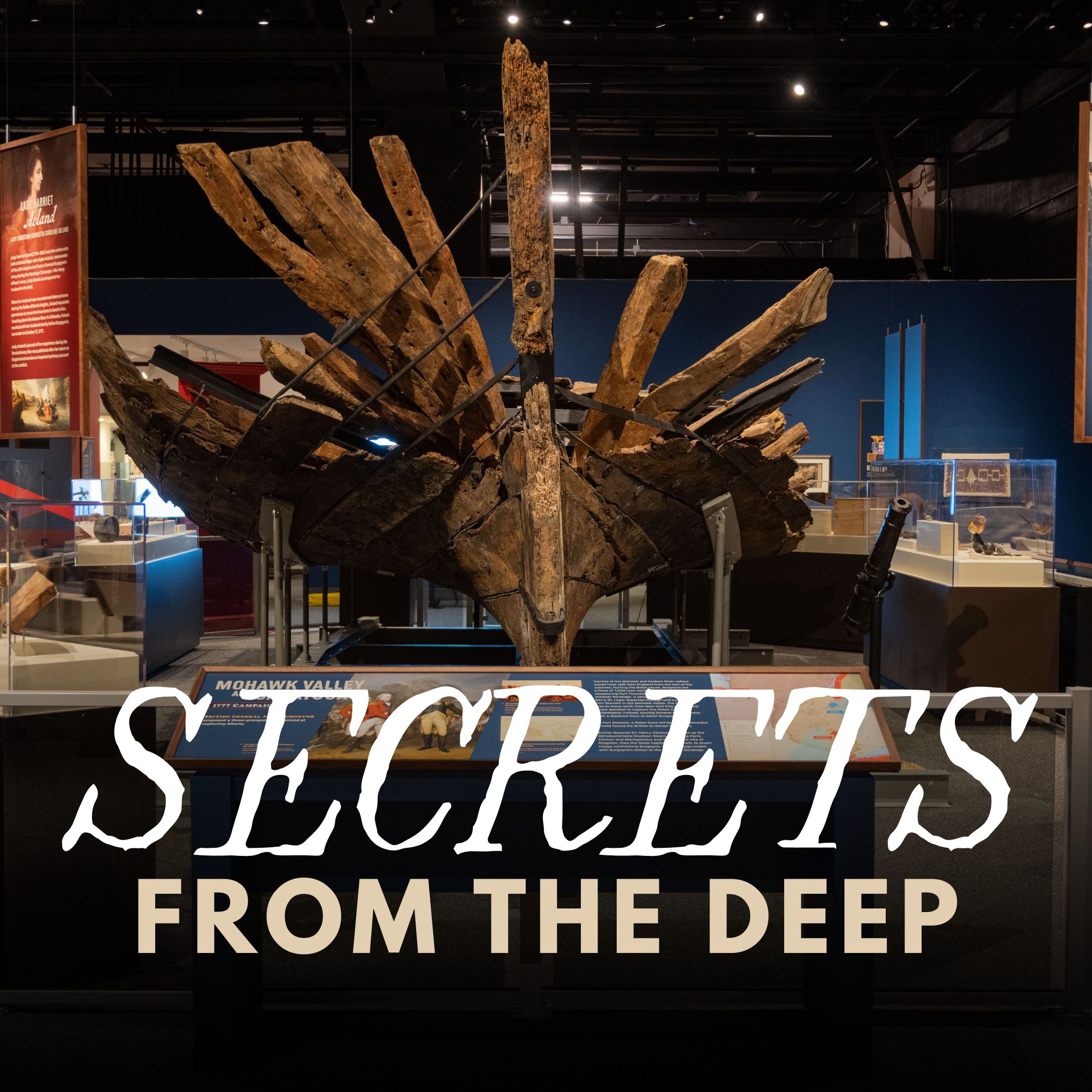 Secrets from the Deep title text over a photograph of the assembled timbers of the Revolutionary War Gunboat on exhibit at the NYSM