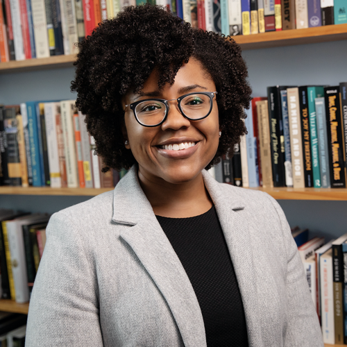 woman wearing glasses standinf infront of a bookcase