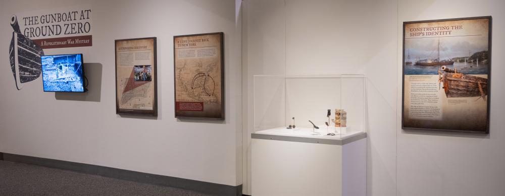 Gallery view of Gunboat to Ground Zero title wall, info panels, and an exhibit case with small artifacts on display