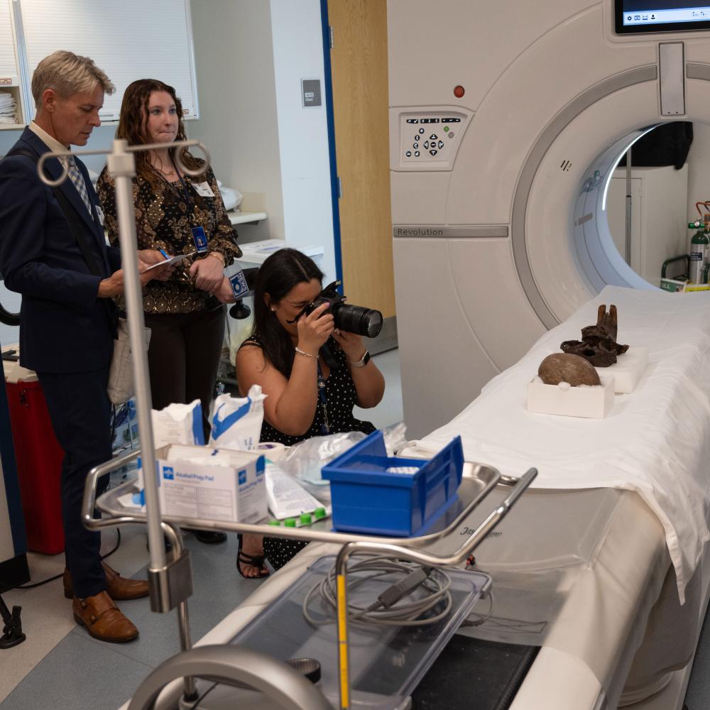 three members of the press take photos of the egg and skull on the CT scanner