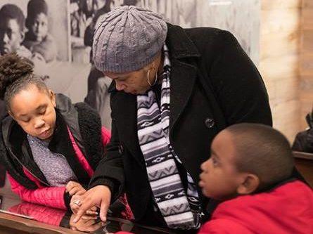 a woman and two children reading a plaque in a museum