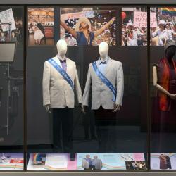 view of exhibit case displaying a vintage opthalmalogy chair, two men's suits with Just Married sashes, and two women's outfits