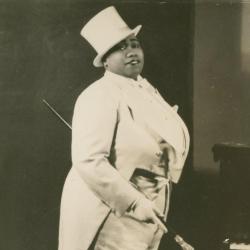 woman in a white suit and jacket with tails and a top hat, carrying a cane with a glass top