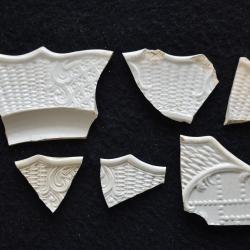 Several molded sherds of white salt-glazed stoneware, all with a dot, diaper and basket pattern. These ceramic artifacts were recovered from a kitchen dump site, likely associated with a 1760s headquarters post. 