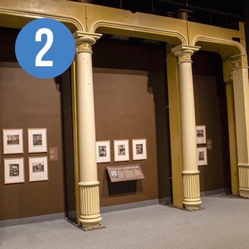 photographs hung on a brown wall in between four sets of pillars