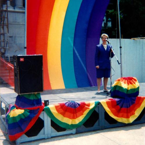 woman standing stage right with a large rainbow flag in the background