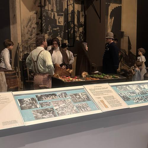 Gallery view of mannequins at an 19th-century market scene behind explainer panels