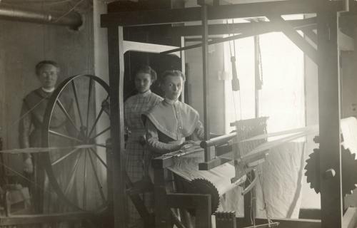 Three women posing near a spinning wheel 