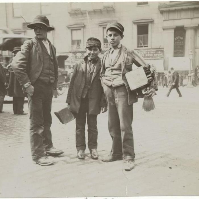 black/white photo of three young boys with boot shining equipment in an urban setting