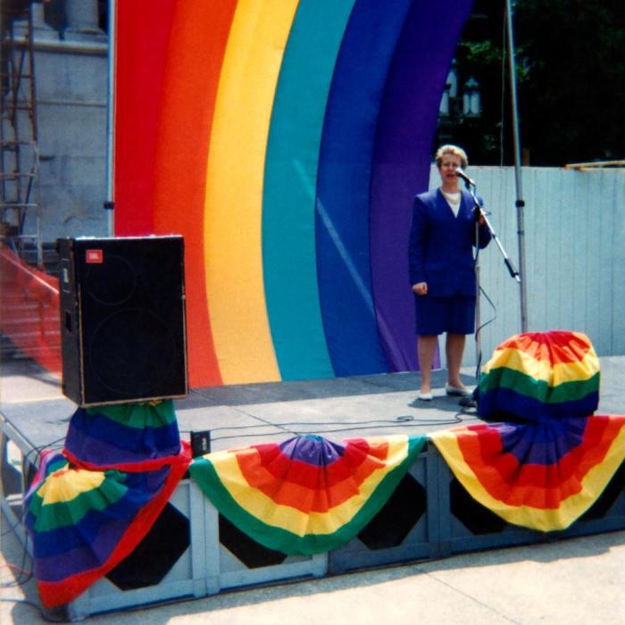 woman standing stage right with a large rainbow flag in the background