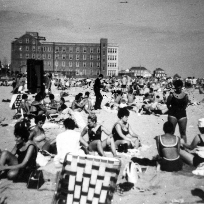 Beach scene with a group of women on the sane and a large hotel in the background
